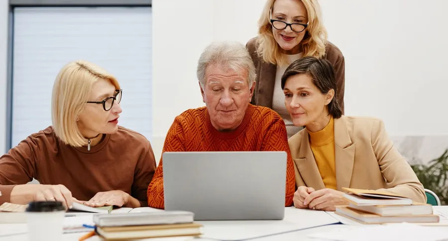 Varias personas adultas consultan juntas un ordenador portátil